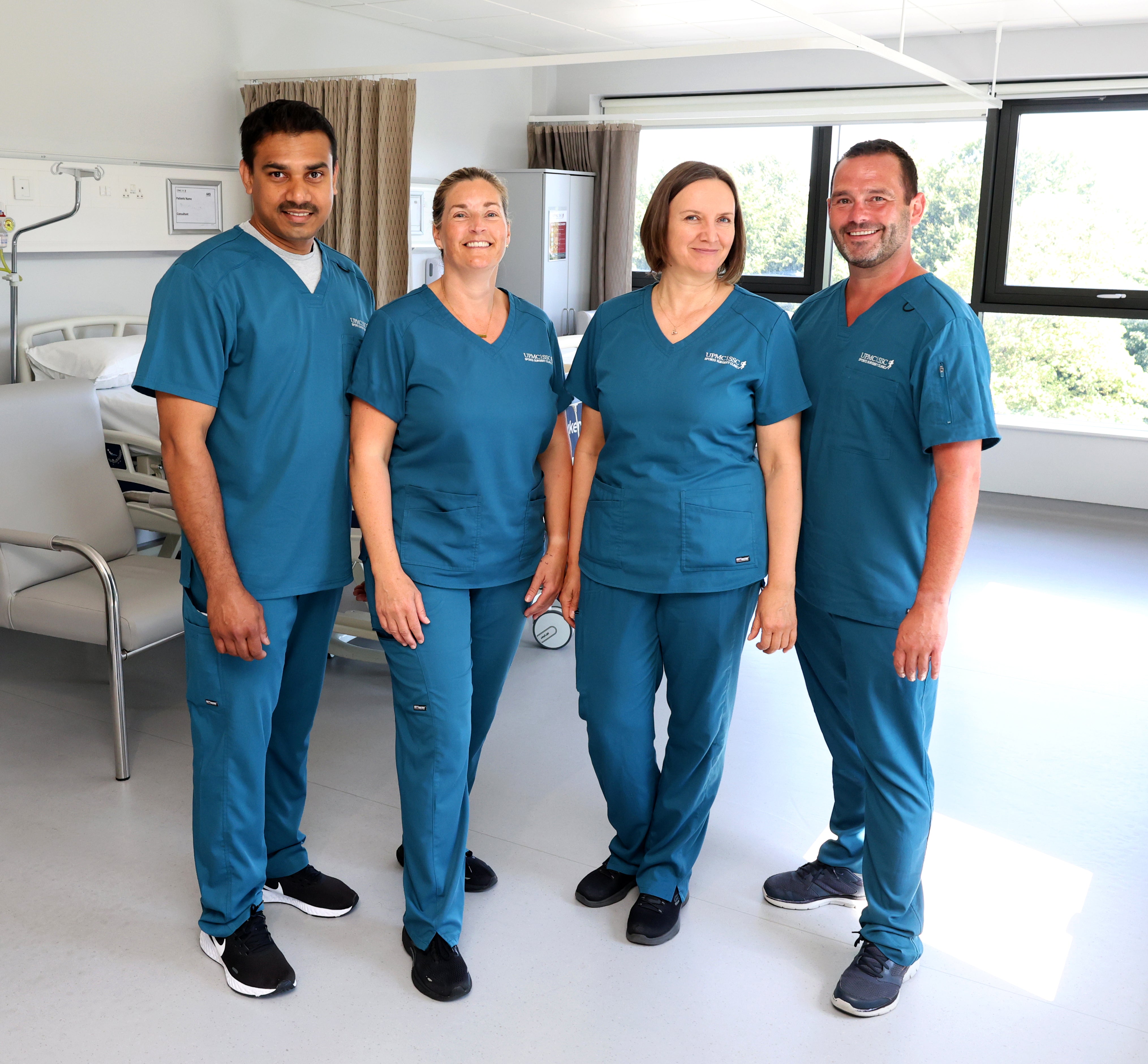 4 medical staff staff wearing caribbean blue scrubs posing in a hospital ward